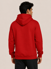 A man viewed from the back wearing a solid red pullover hoodie and black pants, standing against a plain beige studio background.