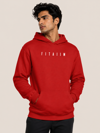 A man wearing a bright red pullover hoodie with the word 'FITAIIM' printed in white block letters across the chest, posed against a solid light beige background.