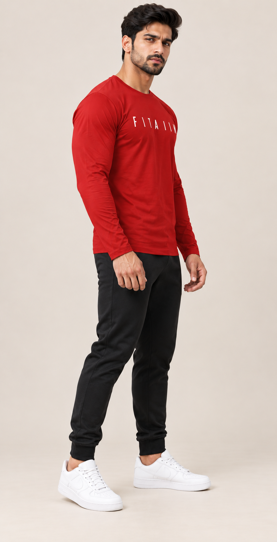A man modeling a red long-sleeve athletic t-shirt with 'FITAIIM' printed in white across the chest, paired with black joggers and white sneakers, against a solid beige studio background.