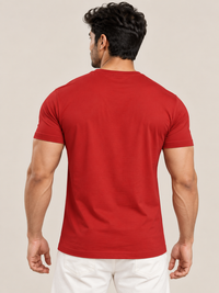 A man viewed from behind wearing a solid red short-sleeve crewneck t-shirt and white pants, set against a plain beige studio background.