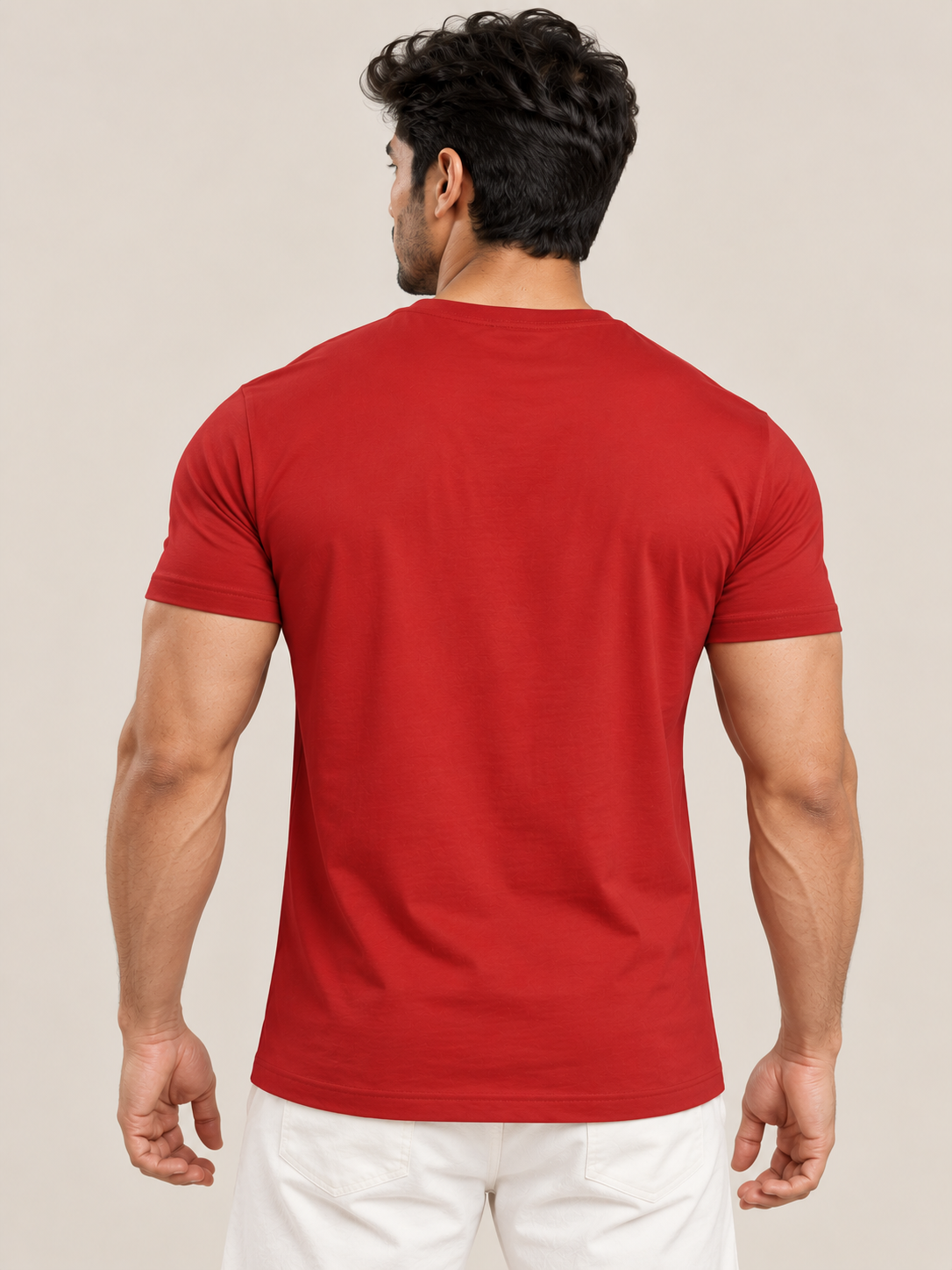 A man viewed from behind wearing a solid red short-sleeve crewneck t-shirt and white pants, set against a plain beige studio background.