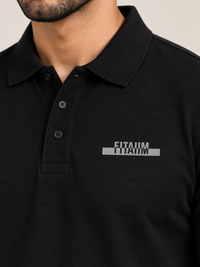 A close-up of a man wearing a BLACK short-sleeve polo shirt with a gray and white 'FITAIIM' graphic printed on the left chest.