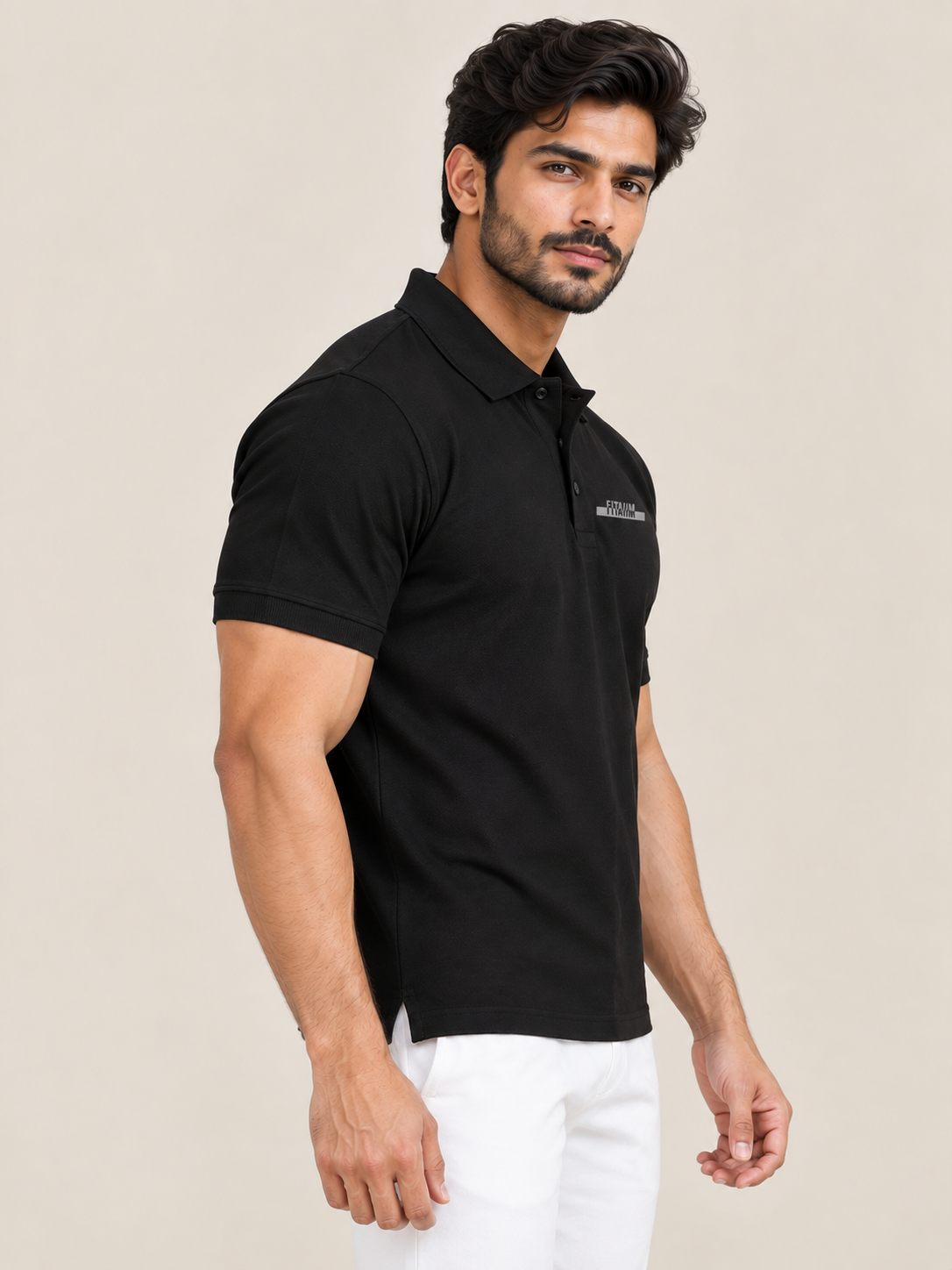 A man wearing a black short-sleeve polo shirt with a small chest logo, paired with white pants, photographed against a plain light beige studio background.