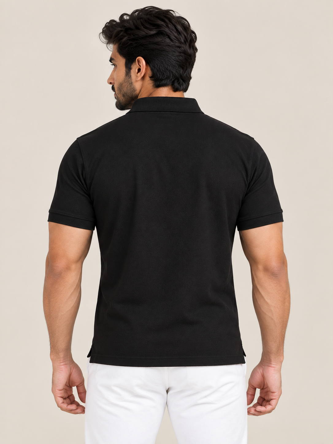 A man viewed from the back wearing a plain black short-sleeve polo shirt and white pants, standing against a light beige studio background.