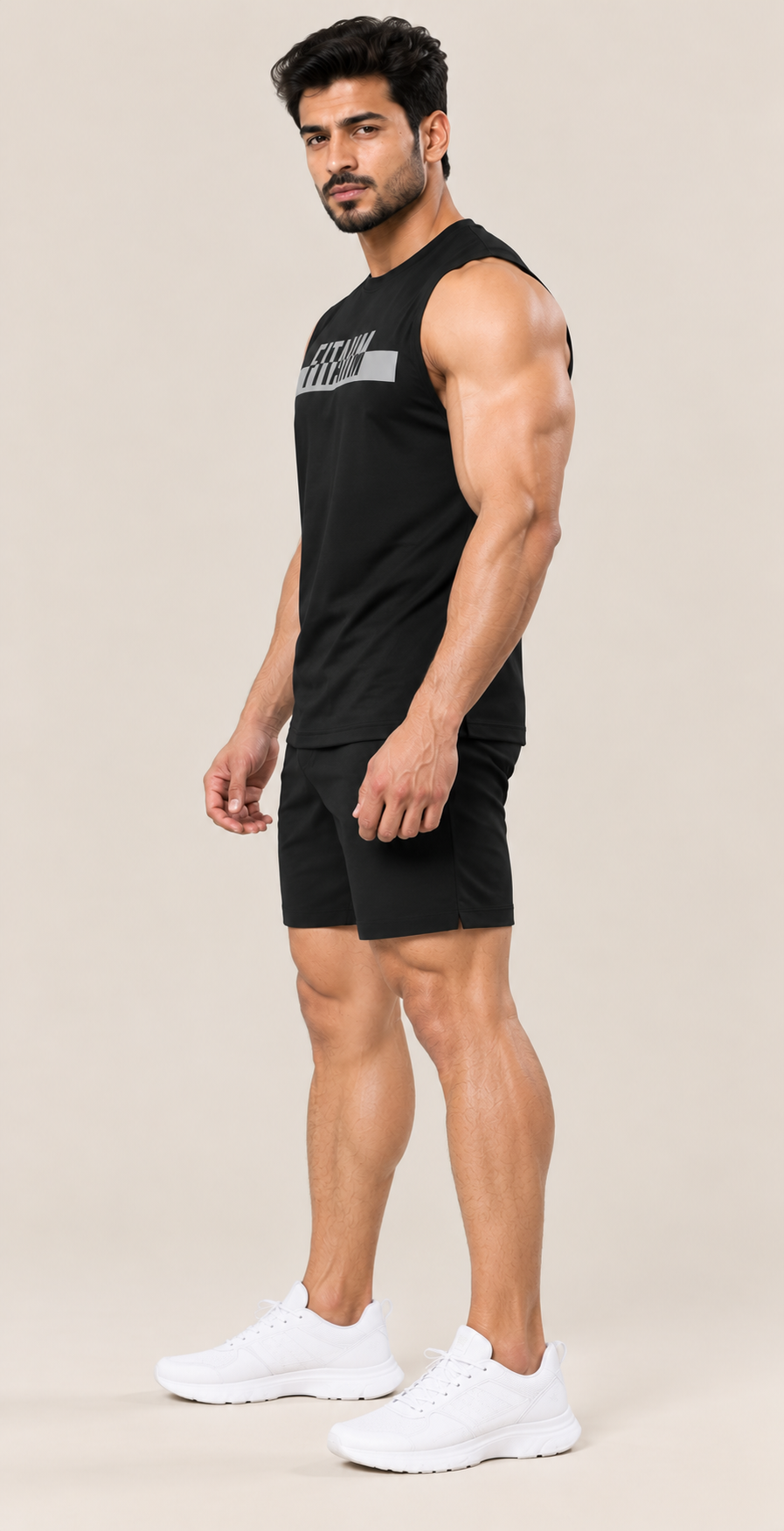 A muscular man modeling a black sleeveless athletic tank top and matching black shorts, paired with white sneakers, against a solid light beige background.