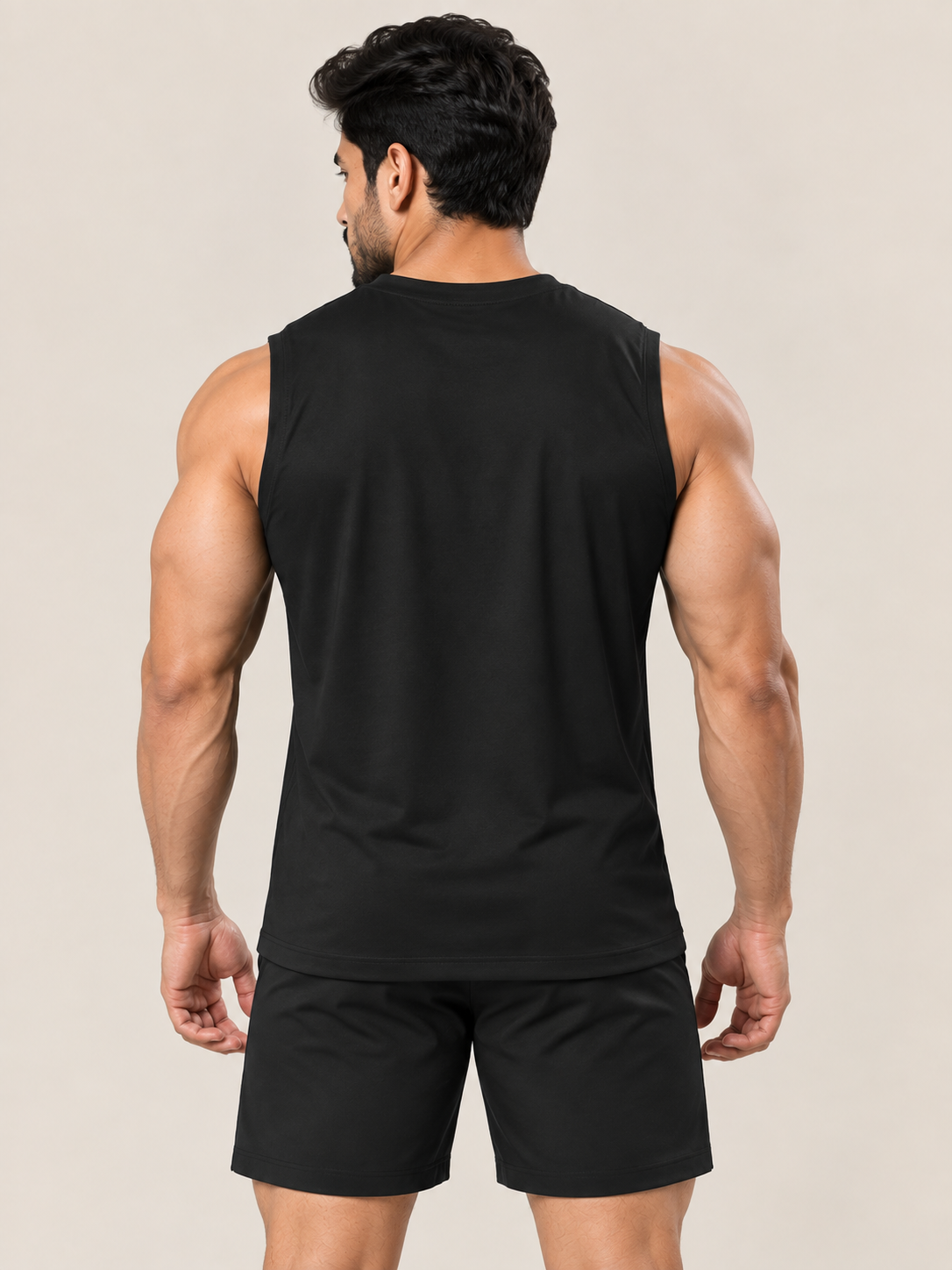 A muscular man shown from the back wearing a black sleeveless athletic tank top and matching black shorts against a solid light beige background.