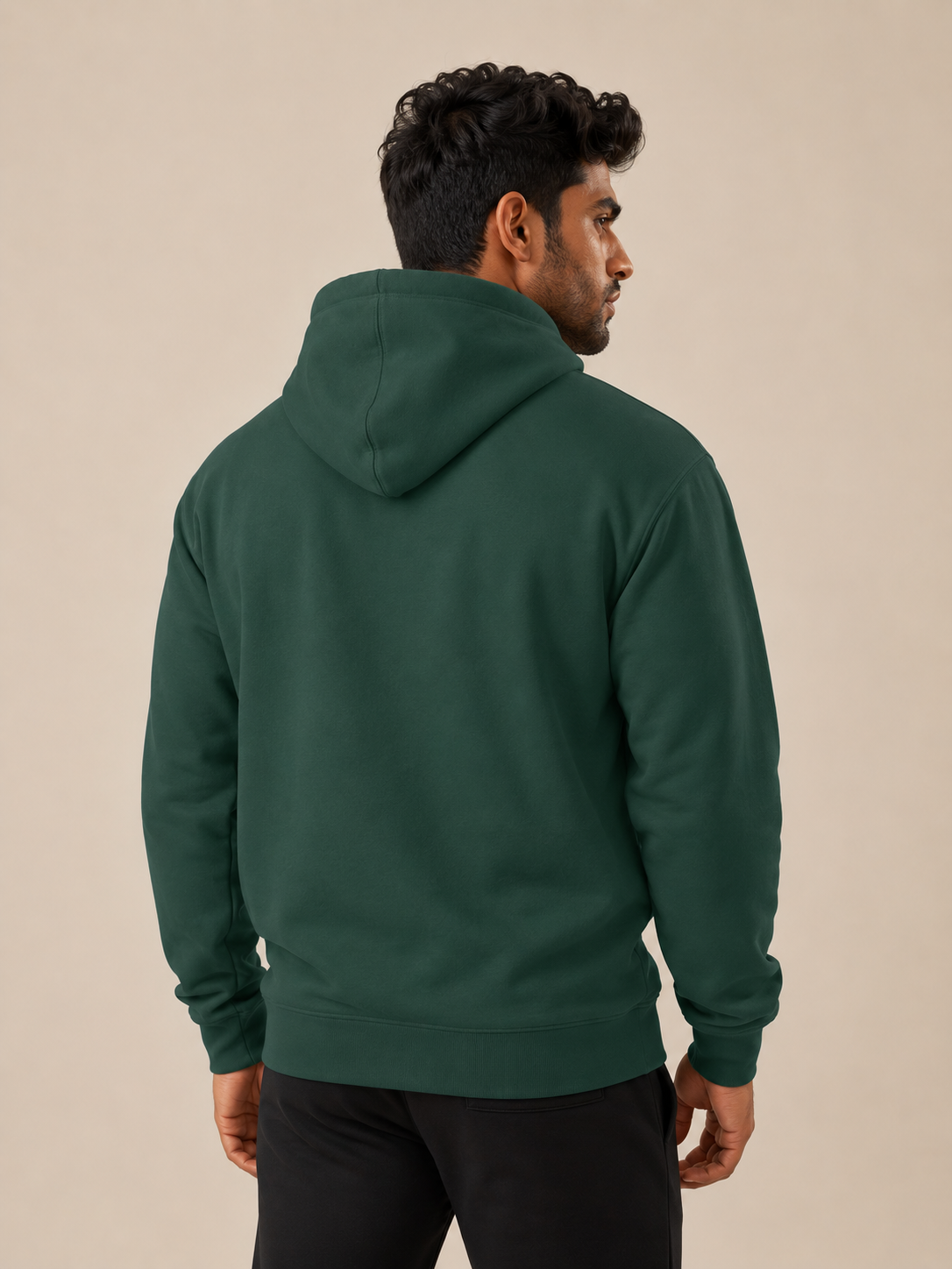 A man wearing a dark green pullover hoodie, shown from the back and side profile against a plain beige studio background.