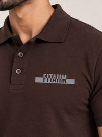 A close-up of a man wearing a dark brown short-sleeve polo shirt with a gray and white 'FITAIIM' graphic printed on the left chest.