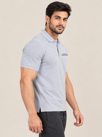 A man wearing a short-sleeve polo shirt in GREY and black pants, standing in profile against a plain beige studio background.