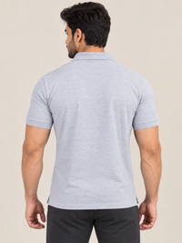 A man wearing a short-sleeve polo shirt in GREY and black pants, standing in profile against a plain beige studio background.