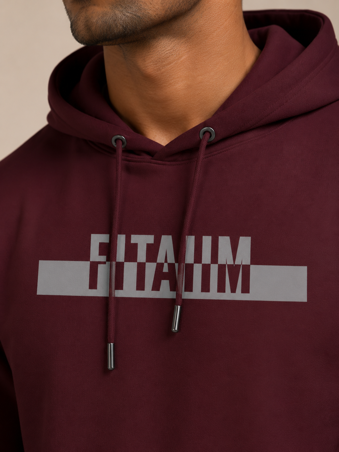 A close-up of a man wearing a maroon hoodie with the name 'FITAIIM' printed in grey capital letters across the chest. The shot focuses on the chest area, showing the drawstrings and the text clearly against a neutral beige background.
