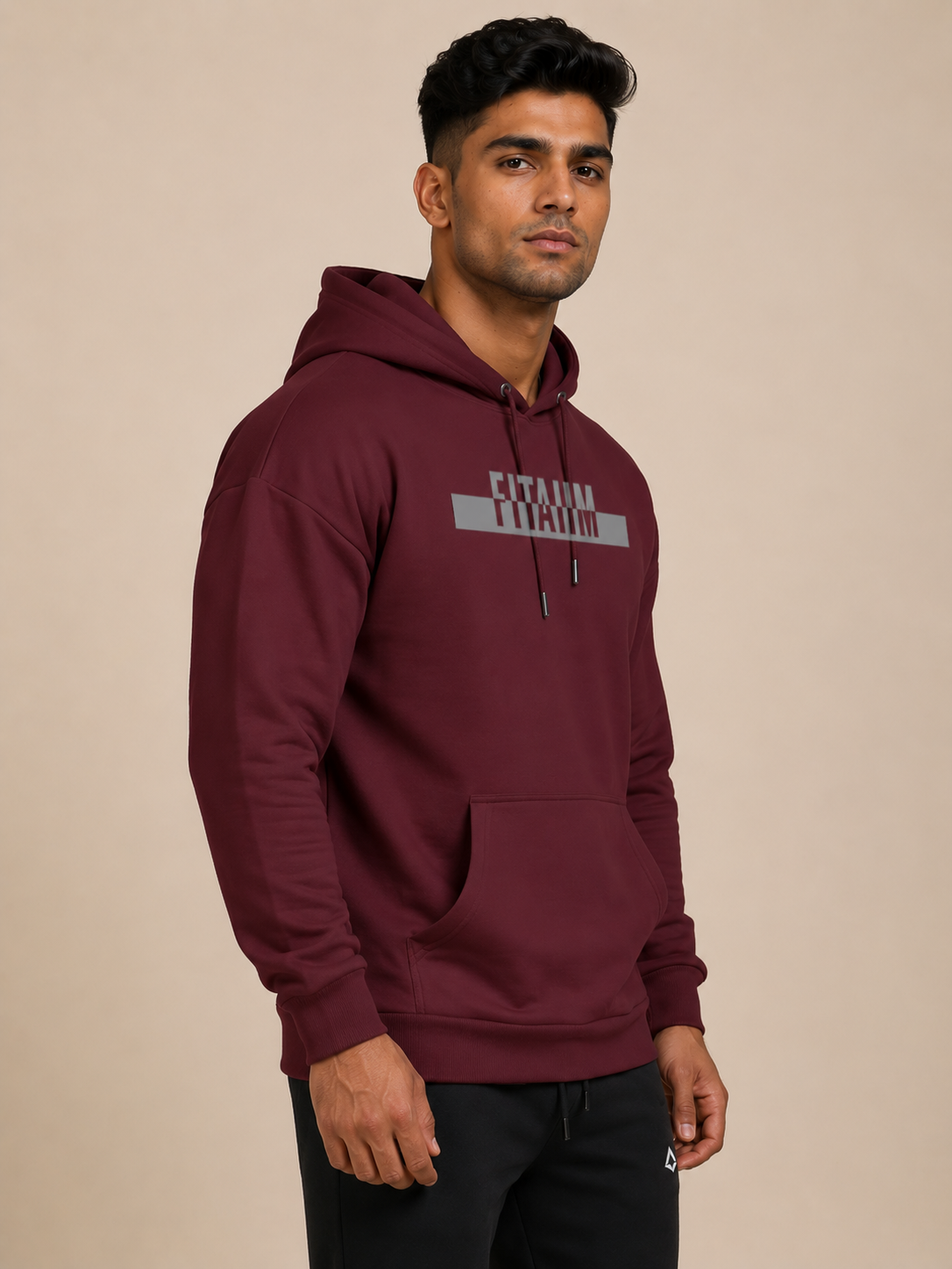 A man wearing a maroon pullover hoodie with 'FITAIIM' printed in grey across the chest, paired with black jogger, against a solid light beige background.