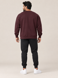 A man shown from the back wearing a matching maroon sweatshirt and jogger pants set, paired with white sneakers, against a solid light beige background.