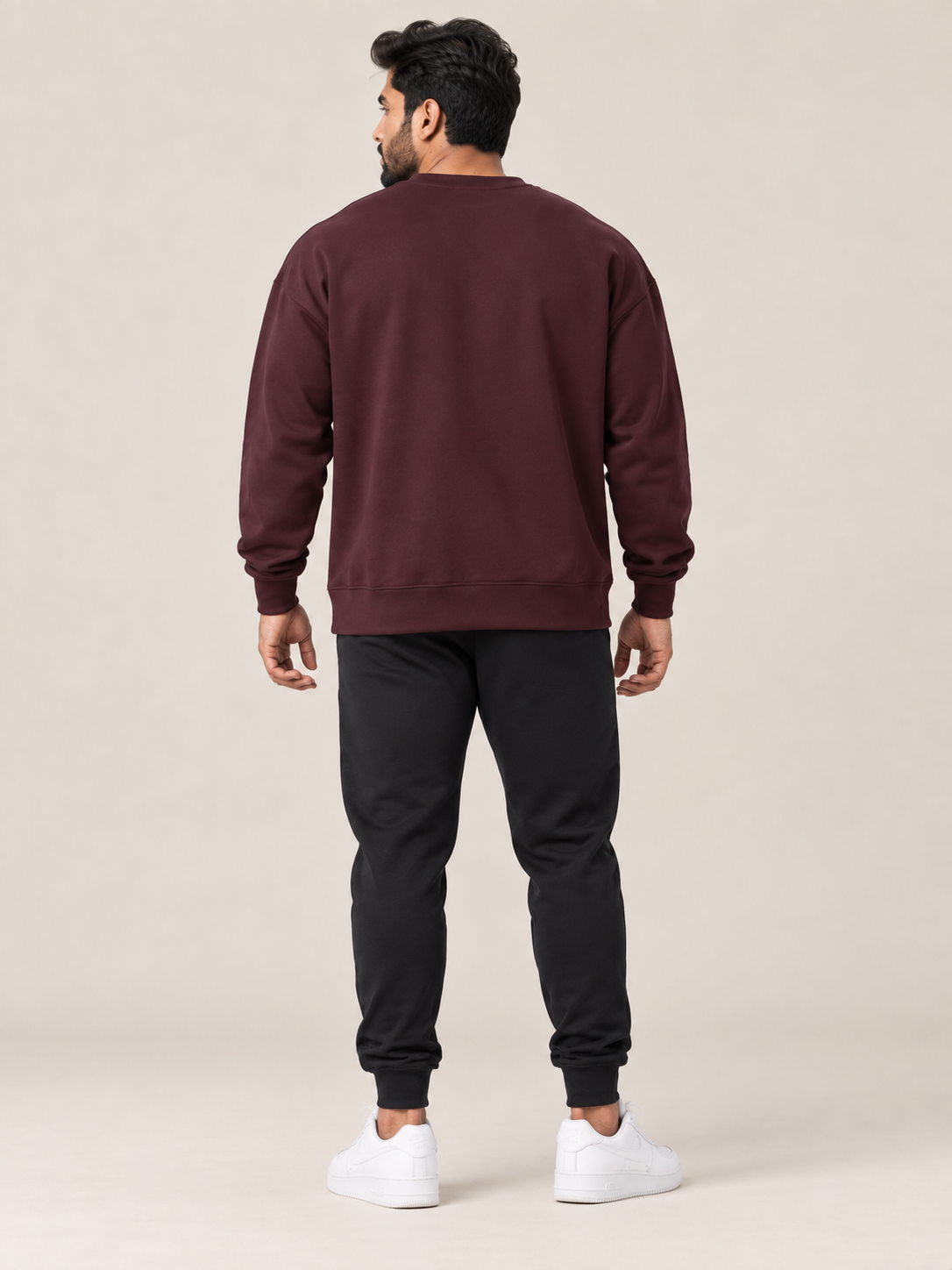 A man shown from the back wearing a matching maroon sweatshirt and jogger pants set, paired with white sneakers, against a solid light beige background.