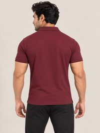 A man shown from the back wearing a MAROON short-sleeve polo shirt, black jogger pants, and white sneakers, standing against a plain beige studio background.