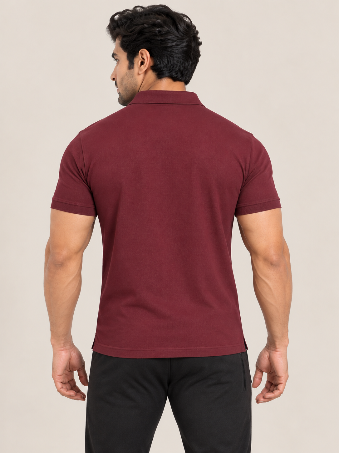 A man shown from the back wearing a MAROON short-sleeve polo shirt, black jogger pants, and white sneakers, standing against a plain beige studio background.