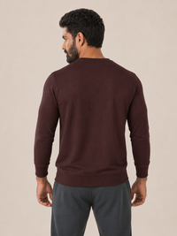 A man viewed from the back wearing a MAROON long-sleeve crewneck sweatshirt and dark gray sweatpants, set against a plain beige studio background.