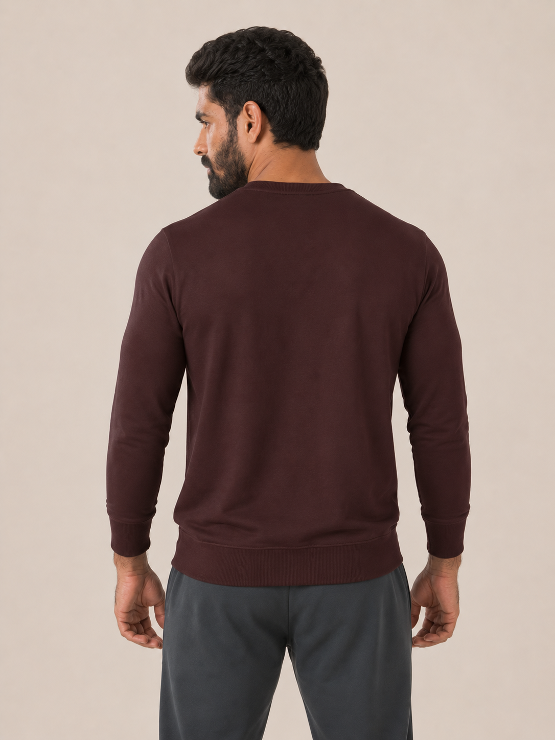 A man viewed from the back wearing a MAROON long-sleeve crewneck sweatshirt and dark gray sweatpants, set against a plain beige studio background.