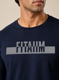 A close-up of a man wearing a navy blue crewneck t-shirt with a large gray graphic on the chest that reads 'FITAIIM'.