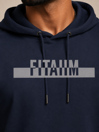A close-up of a person wearing a navy blue hoodie with a gray graphic print on the chest that reads 'FITAIIM.