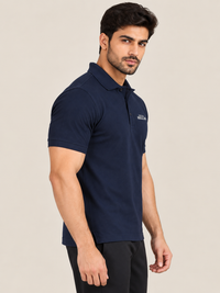 A man wearing a short-sleeve polo shirt in NAVY BLUE and black pants, standing in profile against a plain beige studio background.