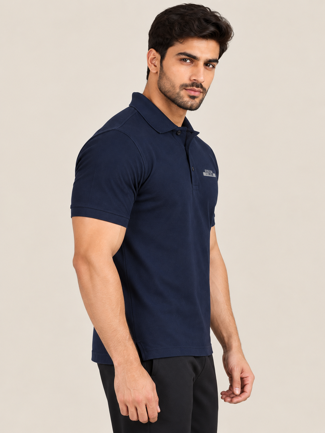 A man wearing a short-sleeve polo shirt in NAVY BLUE and black pants, standing in profile against a plain beige studio background.