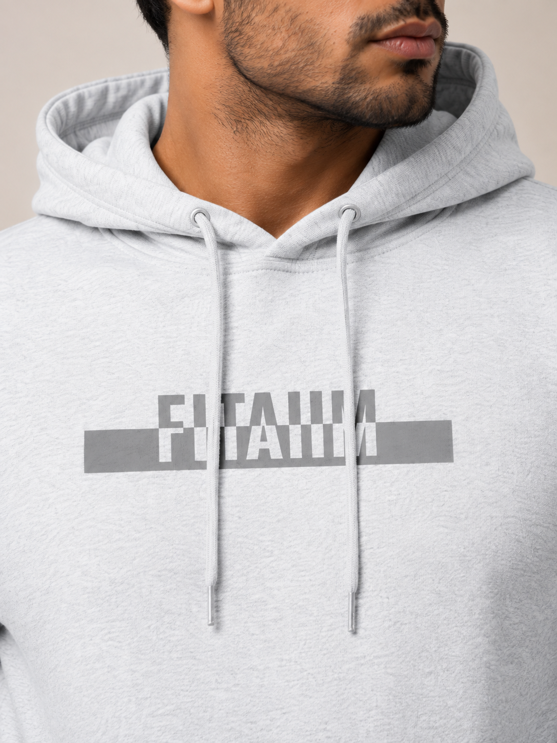 A close-up of a man wearing a light gray heather hoodie with a dark gray graphic print on the chest that reads 'FITAIIM'.